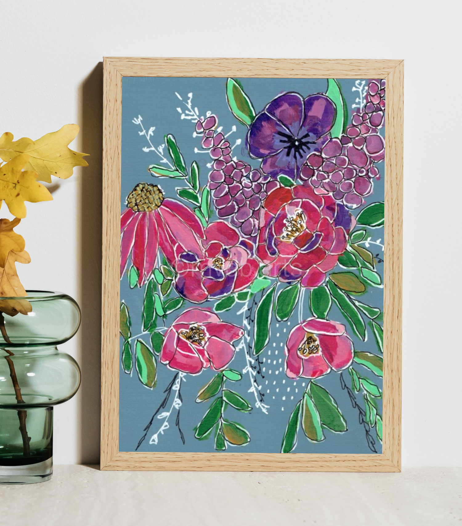 A framed floral art print featuring vibrant pink and purple flowers with green leaves on a dusty blue background, styled in a light wood frame next to a green glass vase with yellow flowers.